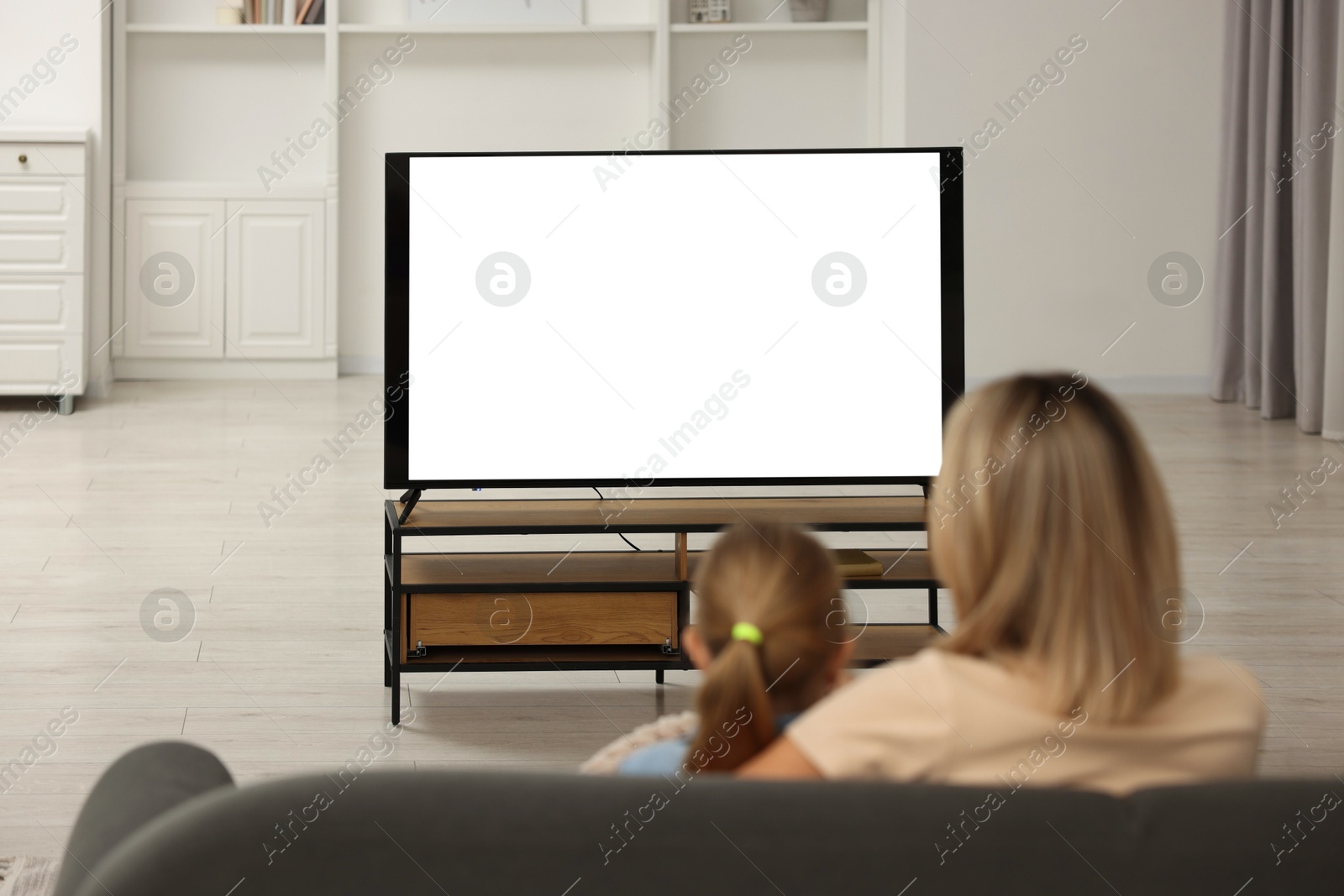 Photo of Mother and her daughter watching TV on sofa at home, back view