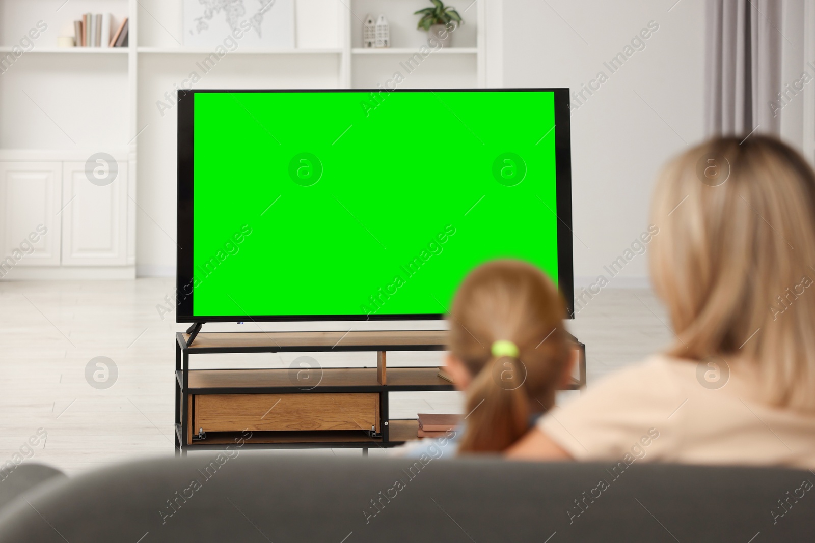 Photo of Mother and her daughter watching TV on sofa at home, back view