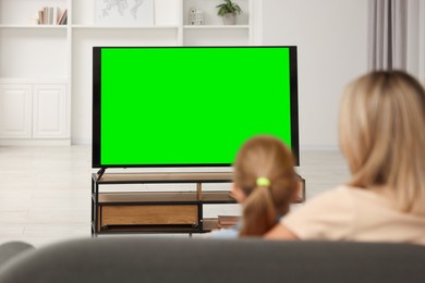 Mother and her daughter watching TV on sofa at home, back view