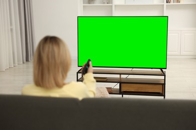 Woman watching TV on sofa at home, back view