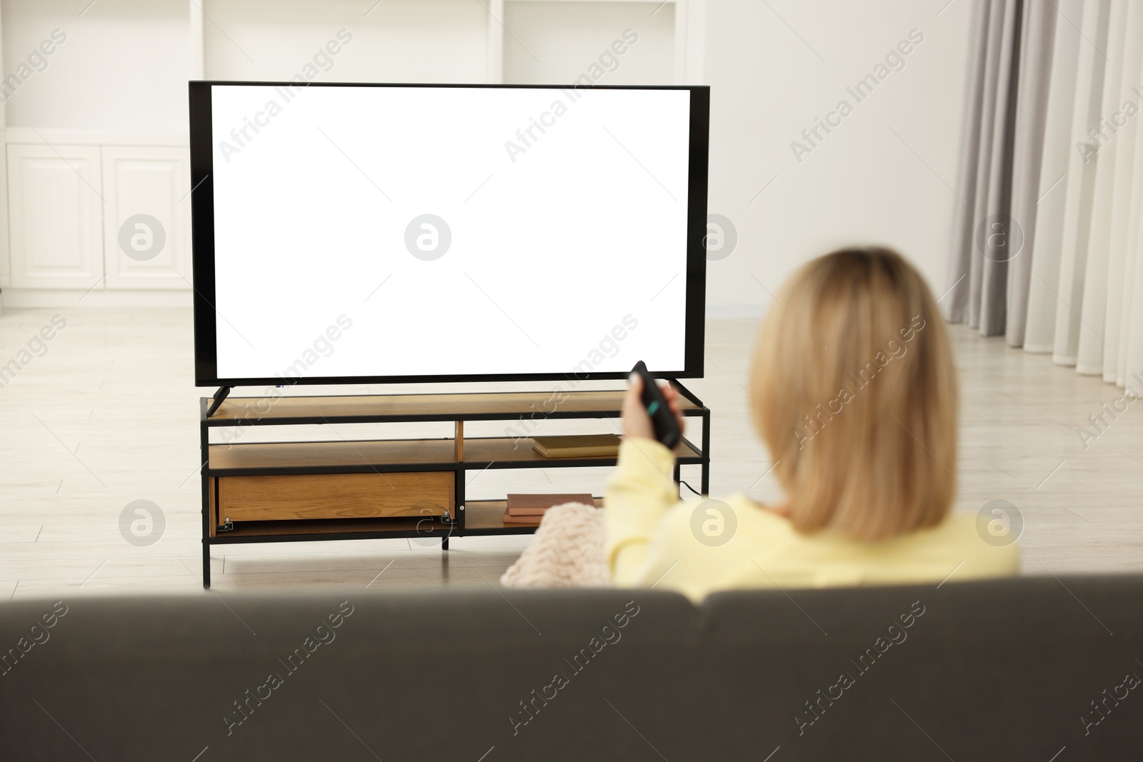 Photo of Woman watching TV on sofa at home, back view