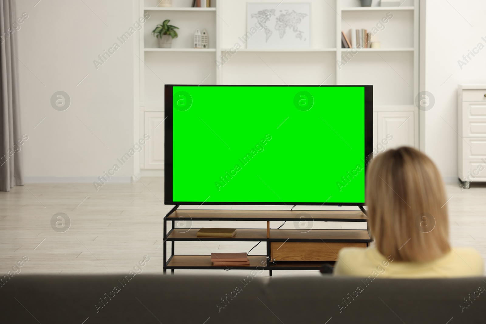 Photo of Woman watching TV on sofa at home, back view