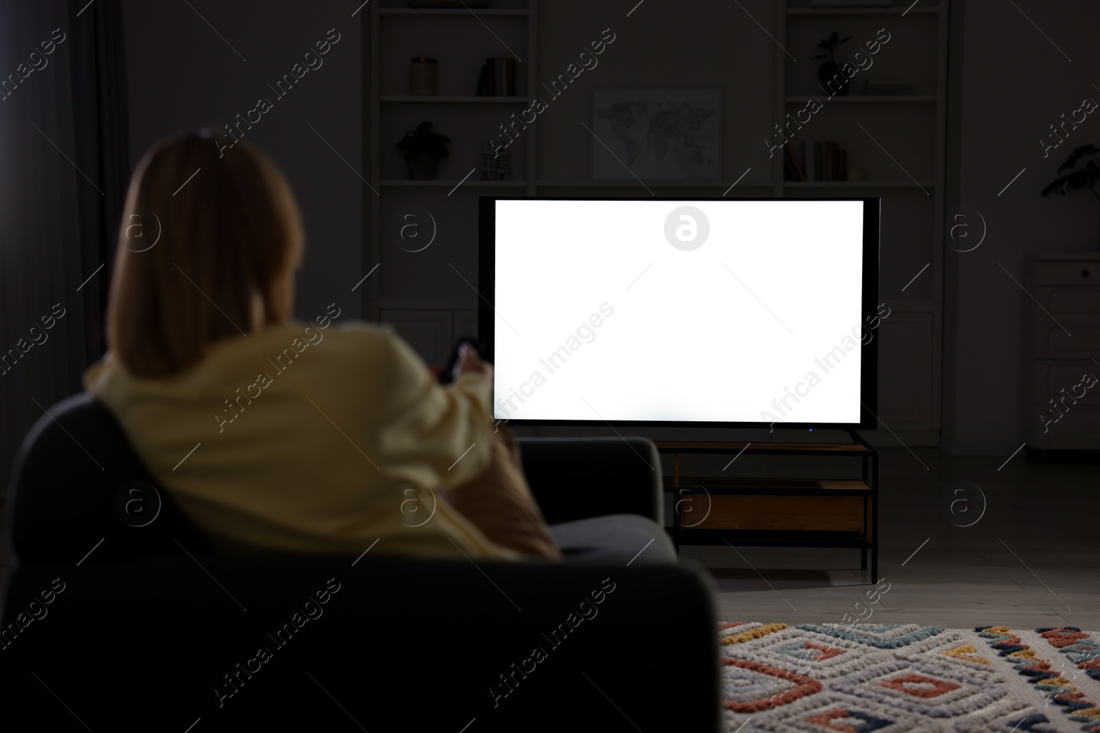 Photo of Woman watching TV on sofa at home in evening, back view