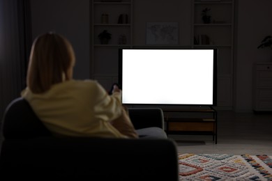 Woman watching TV on sofa at home in evening, back view