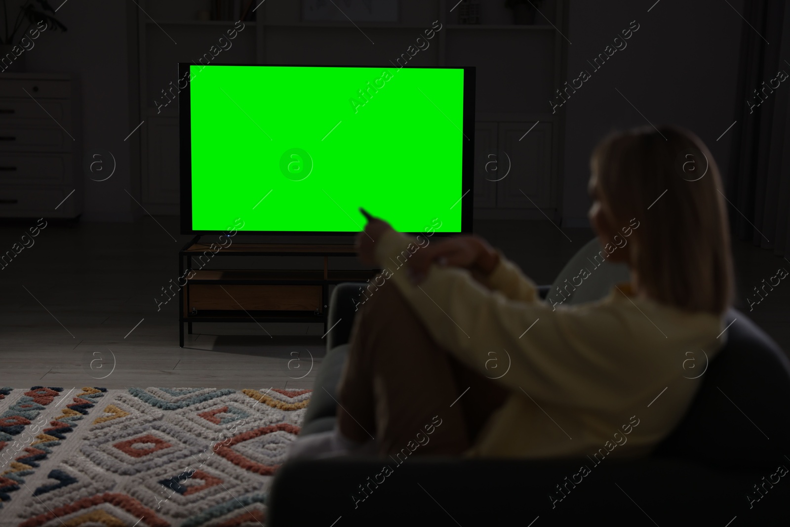 Photo of Woman watching TV on sofa at home in evening