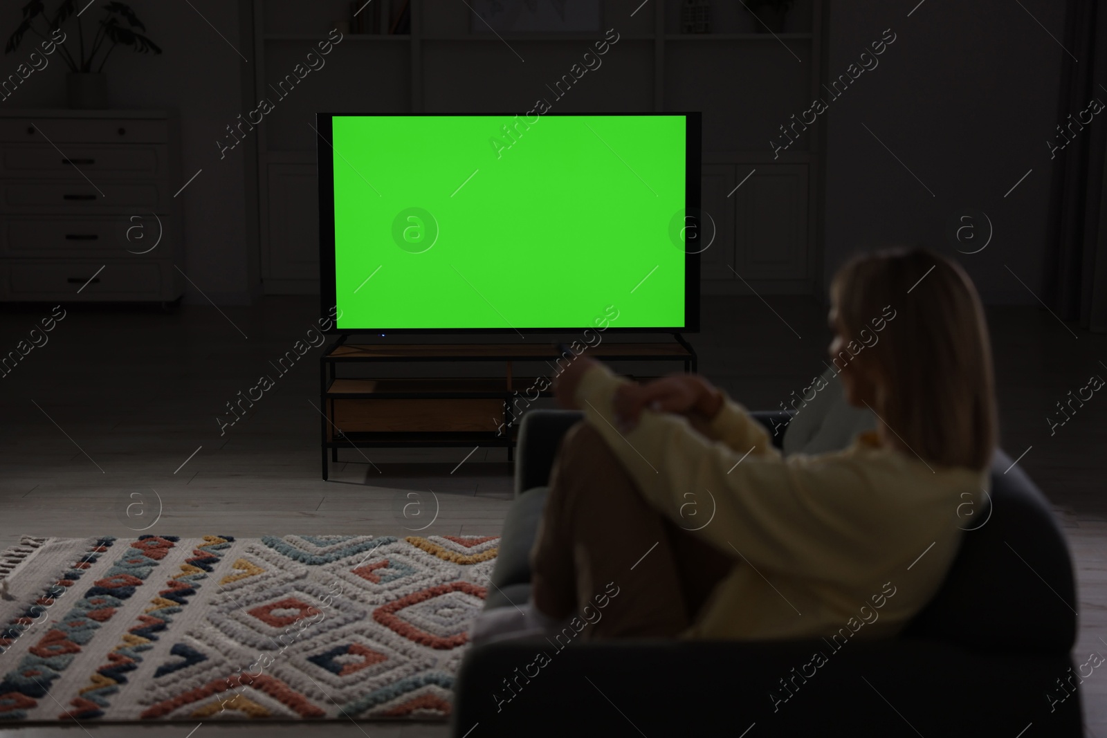 Photo of Woman watching TV on sofa at home in evening