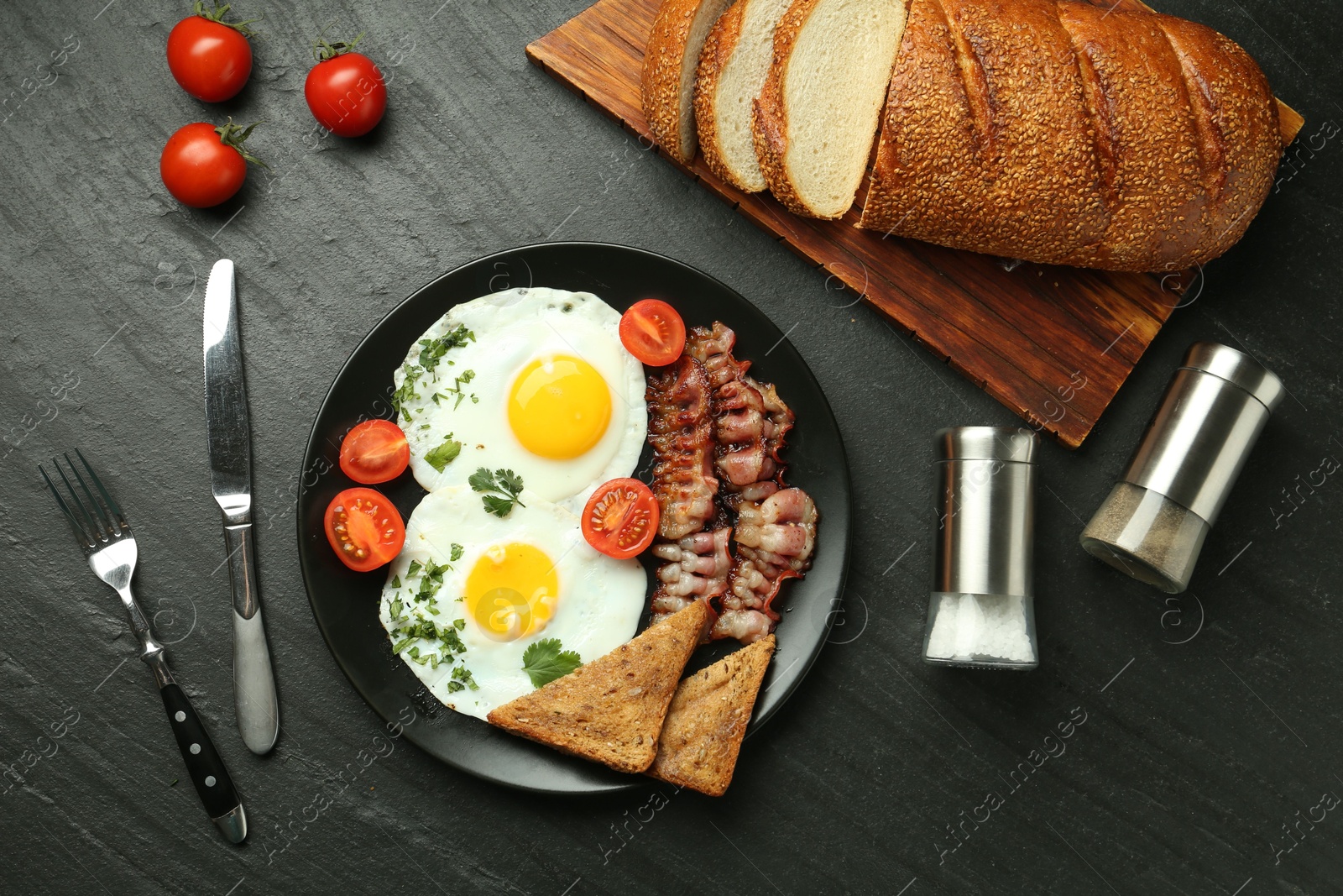 Photo of Tasty brunch. Delicious fried eggs, bacon and pieces of toast served on black table, flat lay