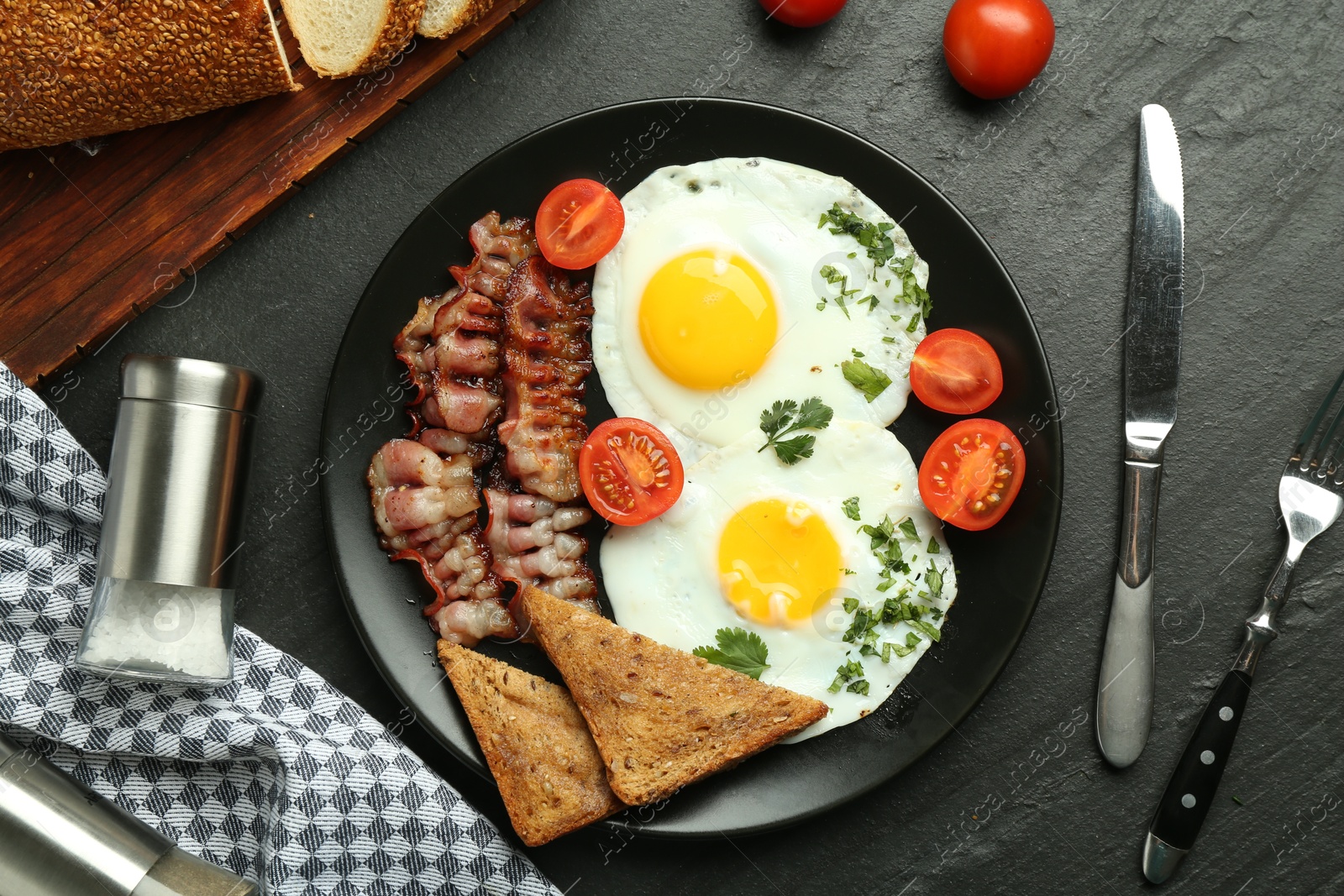 Photo of Tasty brunch. Delicious fried eggs, bacon and pieces of toast served on black table, flat lay