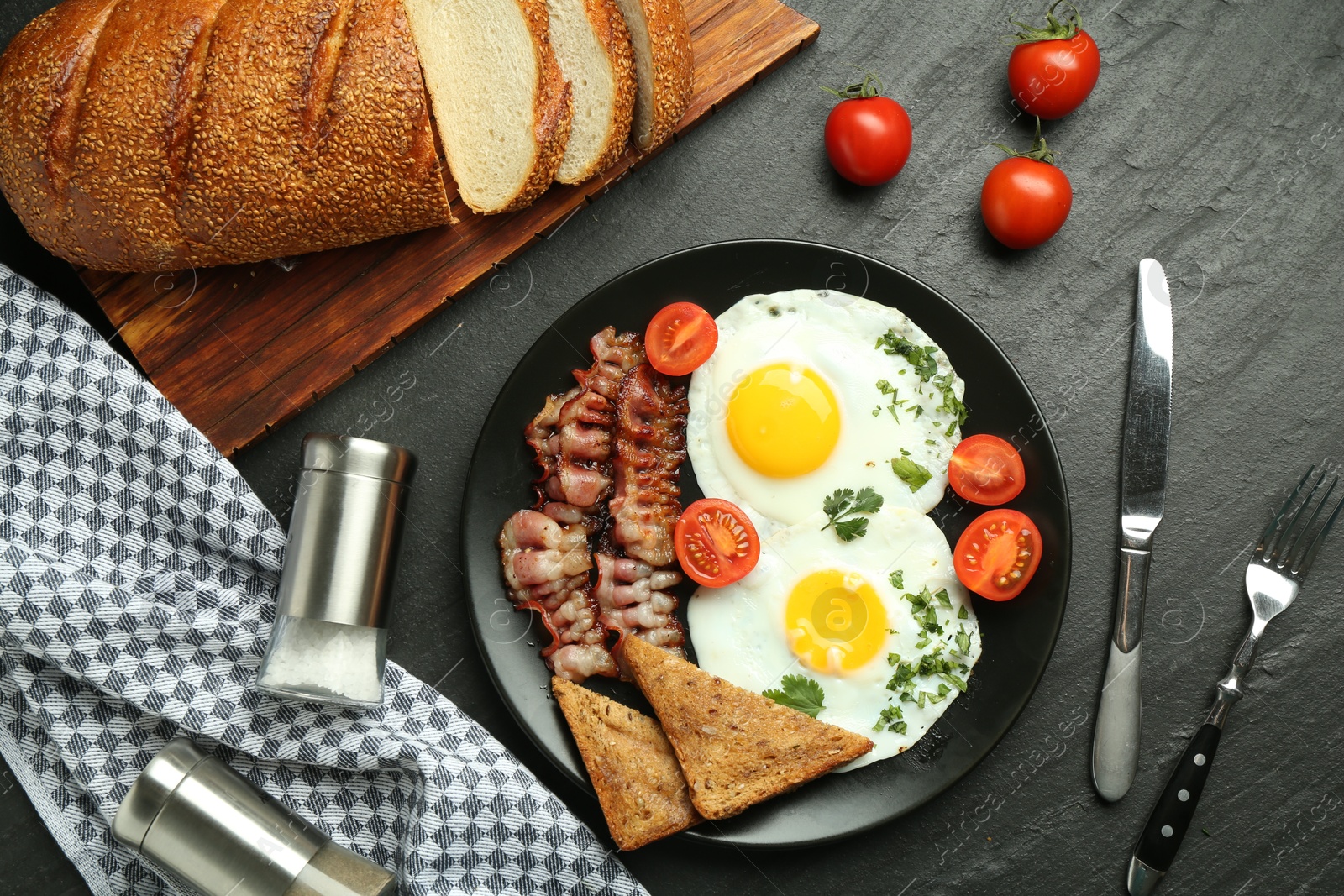 Photo of Tasty brunch. Delicious fried eggs, bacon and pieces of toast served on black table, flat lay