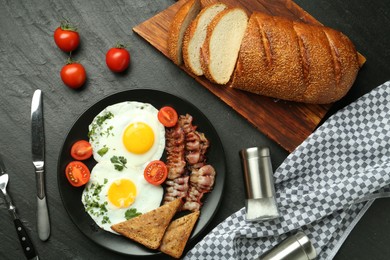 Photo of Tasty brunch. Delicious fried eggs, bacon and pieces of toast served on black table, flat lay