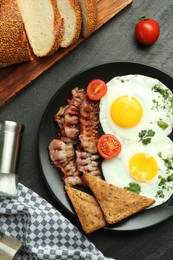 Photo of Tasty brunch. Delicious fried eggs, bacon and pieces of toast served on black table, flat lay