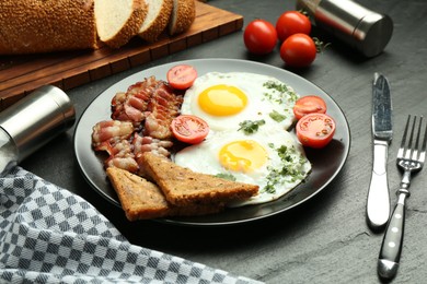 Photo of Tasty brunch. Delicious fried eggs, bacon and pieces of toast served on black table