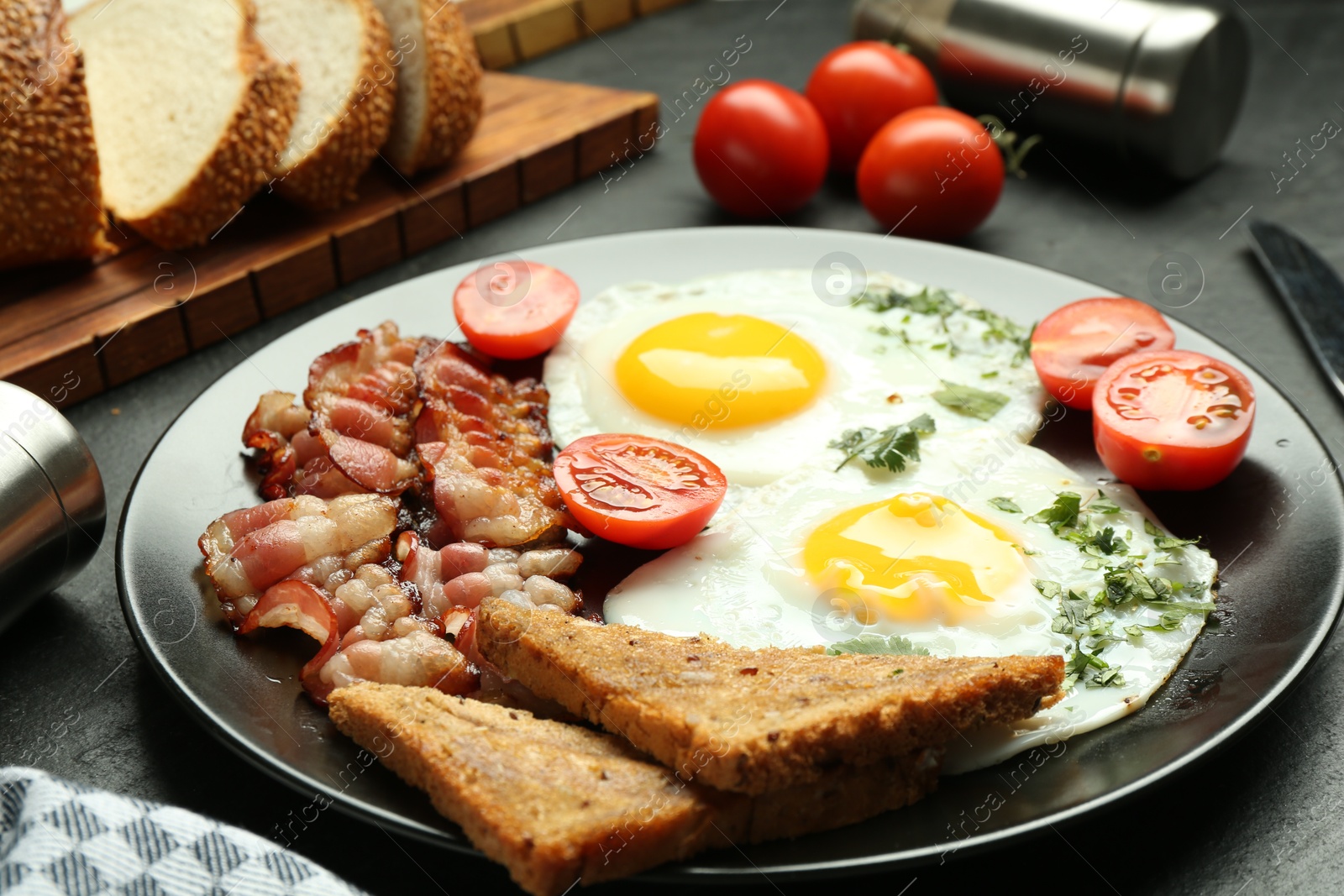 Photo of Tasty brunch. Delicious fried eggs, bacon and pieces of toast served on black table, closeup