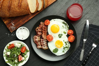 Photo of Tasty brunch. Delicious fried eggs, bacon, salad and glass of juice served on black table, flat lay