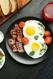 Photo of Tasty brunch. Delicious fried eggs, bacon and glass of juice served on black table, flat lay