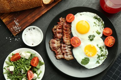 Photo of Tasty brunch. Delicious fried eggs, bacon, salad and glass of juice served on black table, flat lay