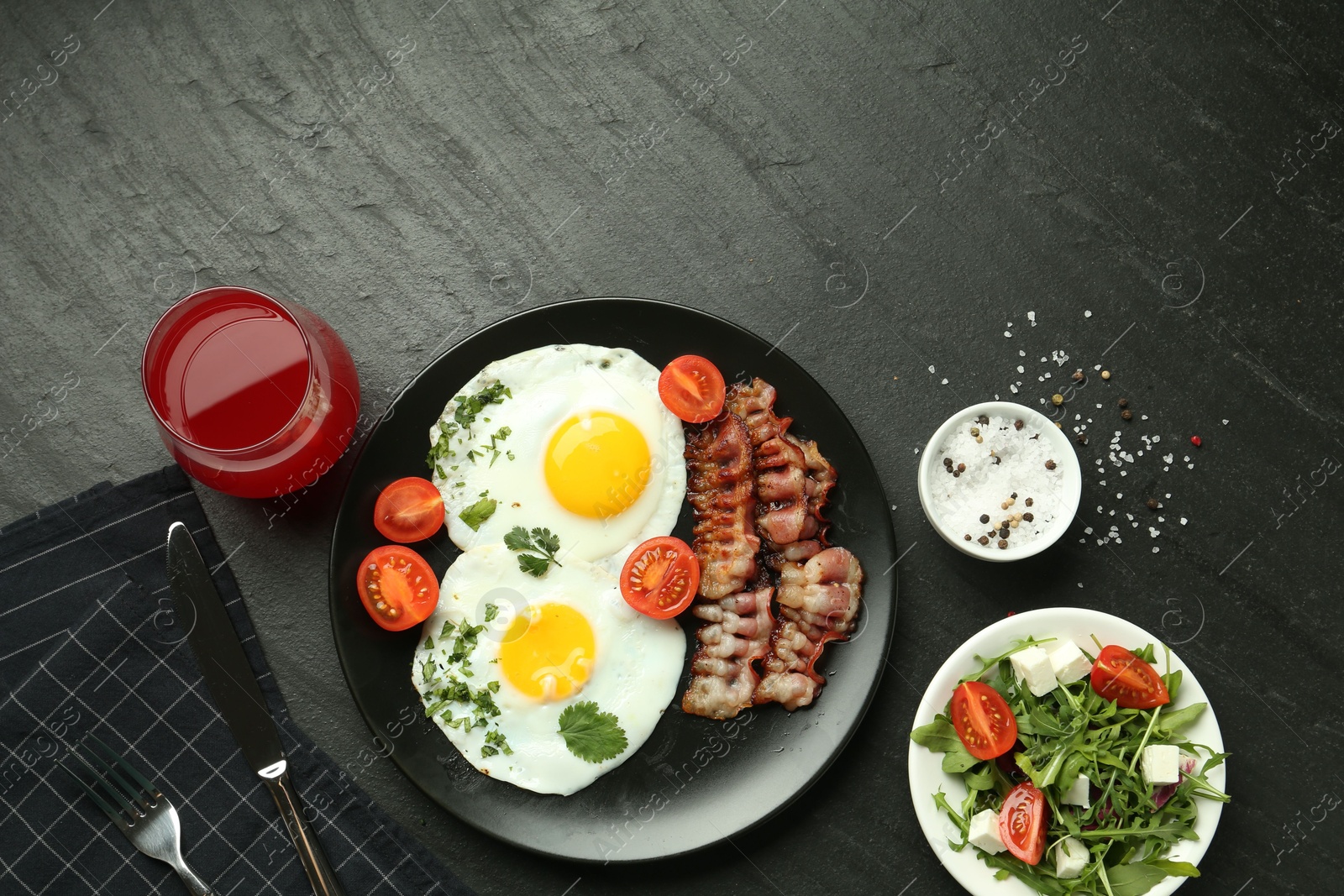 Photo of Tasty brunch. Delicious fried eggs, bacon, salad and glass of juice served on black table, flat lay. Space for text