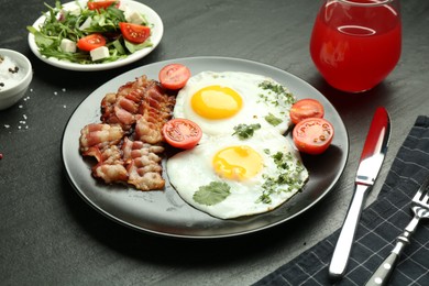 Photo of Tasty brunch. Delicious fried eggs, bacon, salad and glass of juice served on black table