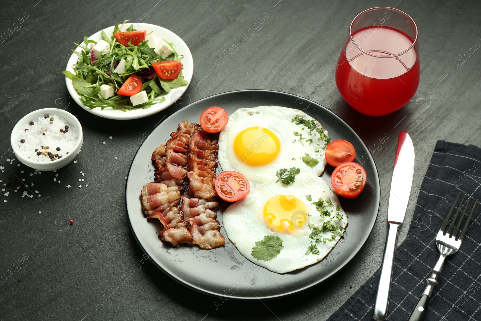 Photo of Tasty brunch. Delicious fried eggs, bacon, salad and glass of juice served on black table