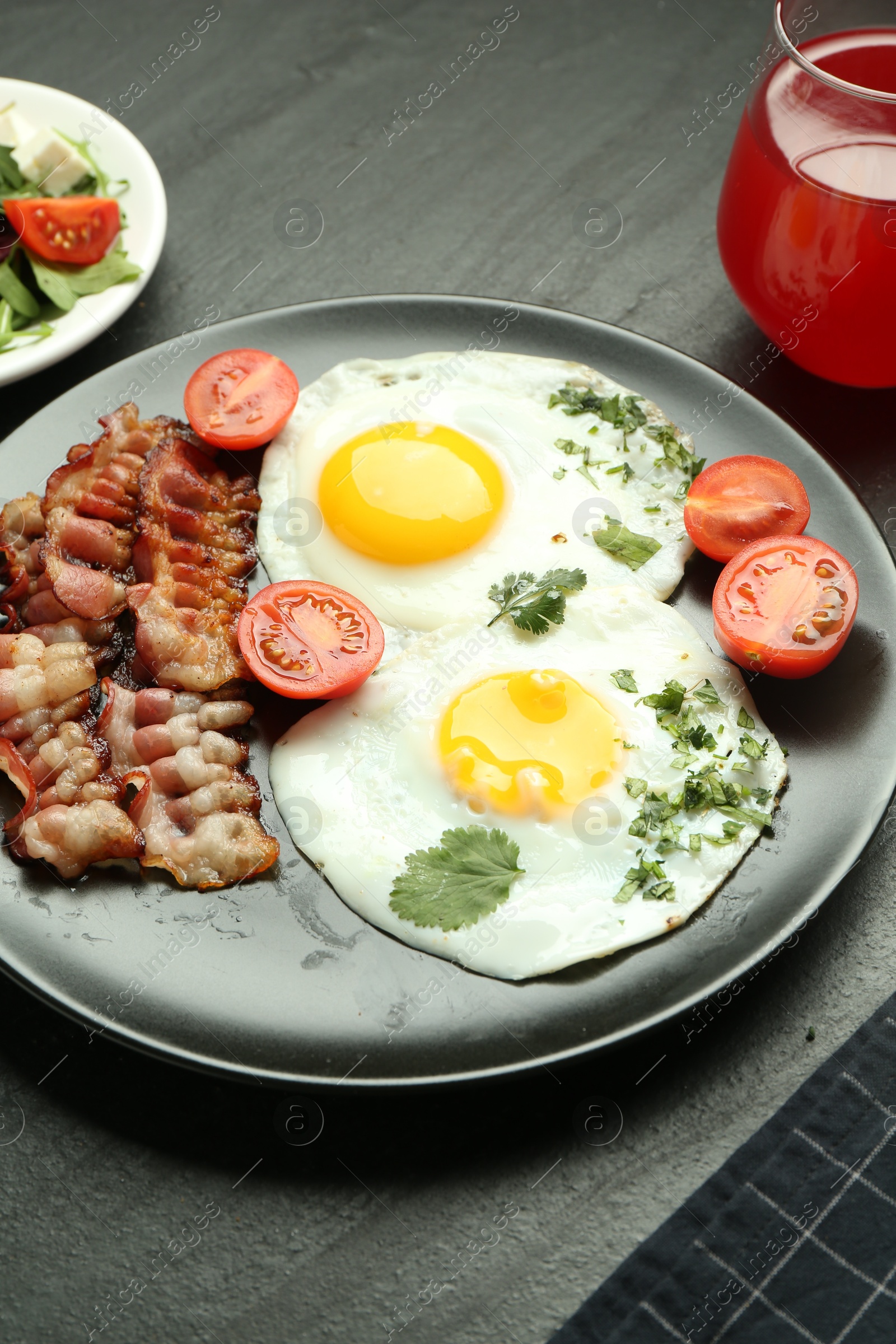 Photo of Tasty brunch. Delicious fried eggs, bacon, tomatoes and juice served on black table, closeup