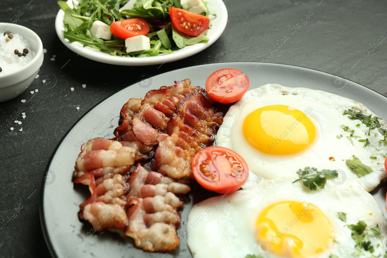 Photo of Tasty brunch. Delicious fried eggs, bacon and salad served on black table, closeup