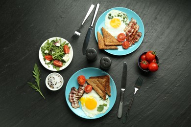 Photo of Tasty brunch. Delicious fried eggs, bacon, pieces of toast and salad served on black table, flat lay