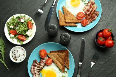 Photo of Tasty brunch. Delicious fried eggs, bacon, pieces of toast and salad served on black table, flat lay