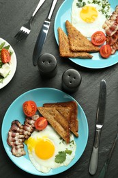 Photo of Tasty brunch. Delicious fried eggs, bacon, pieces of toast and salad served on black table, flat lay