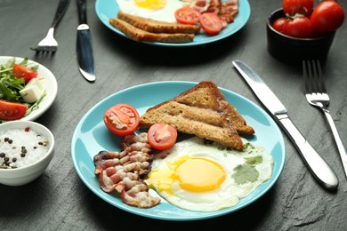 Photo of Tasty brunch. Delicious fried eggs, bacon, pieces of toast and salad served on black table, closeup