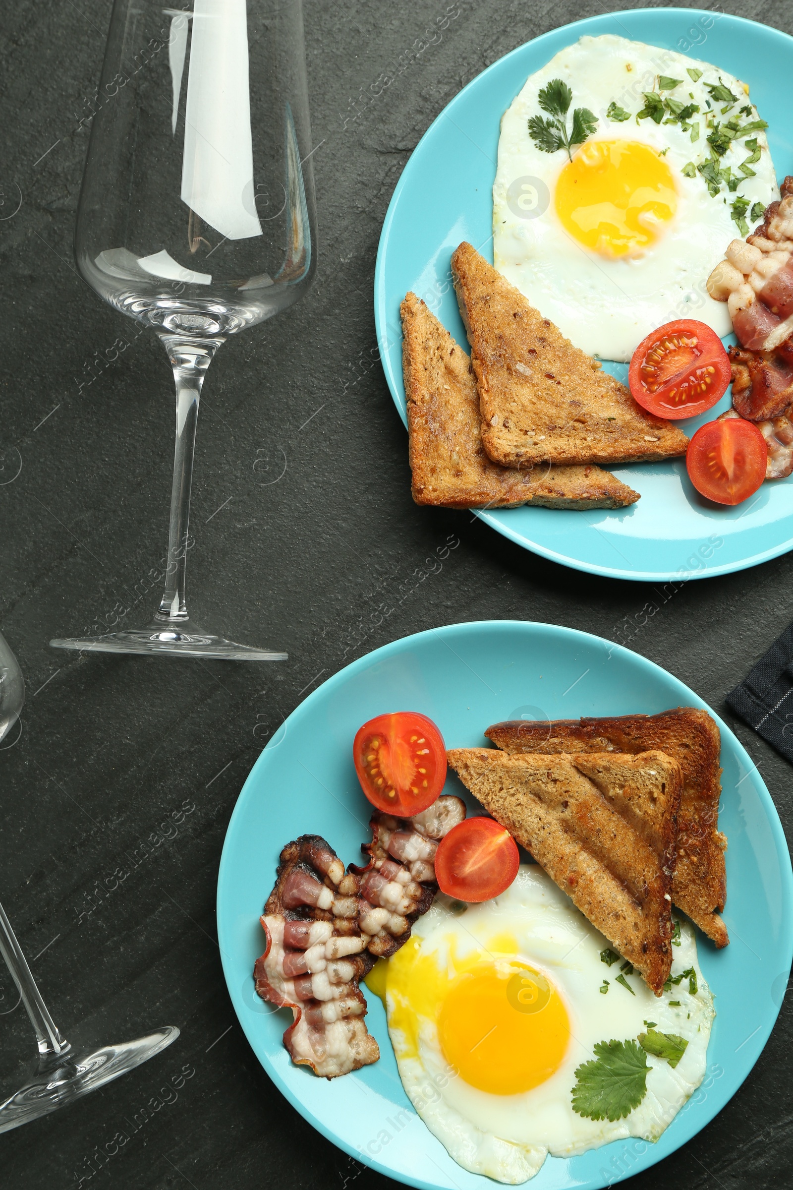 Photo of Delicious fried eggs, bacon and pieces of toast served for brunch on black table, flat lay