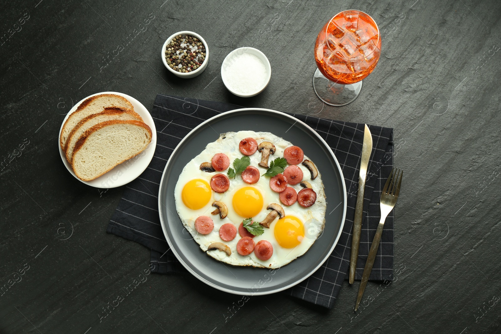 Photo of Tasty brunch. Delicious fried eggs with sausage and mushrooms served on black table, flat lay