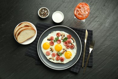 Photo of Tasty brunch. Delicious fried eggs with sausage and mushrooms served on black table, flat lay