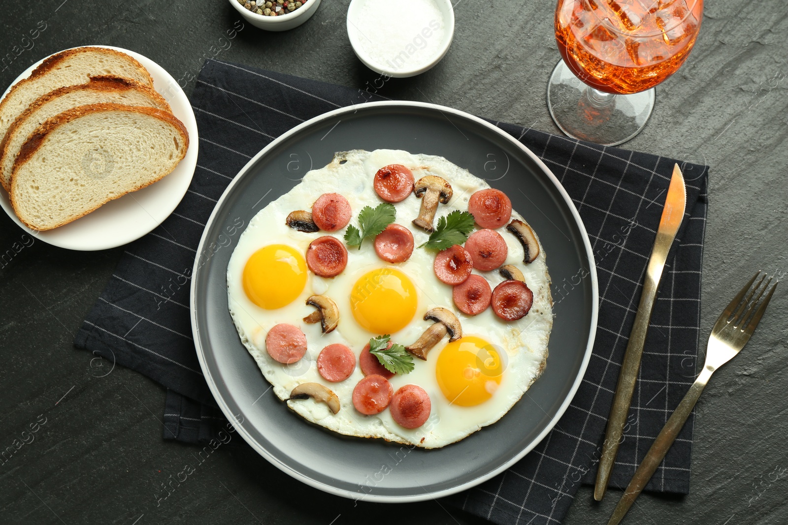 Photo of Tasty brunch. Delicious fried eggs with sausage and mushrooms served on black table, flat lay