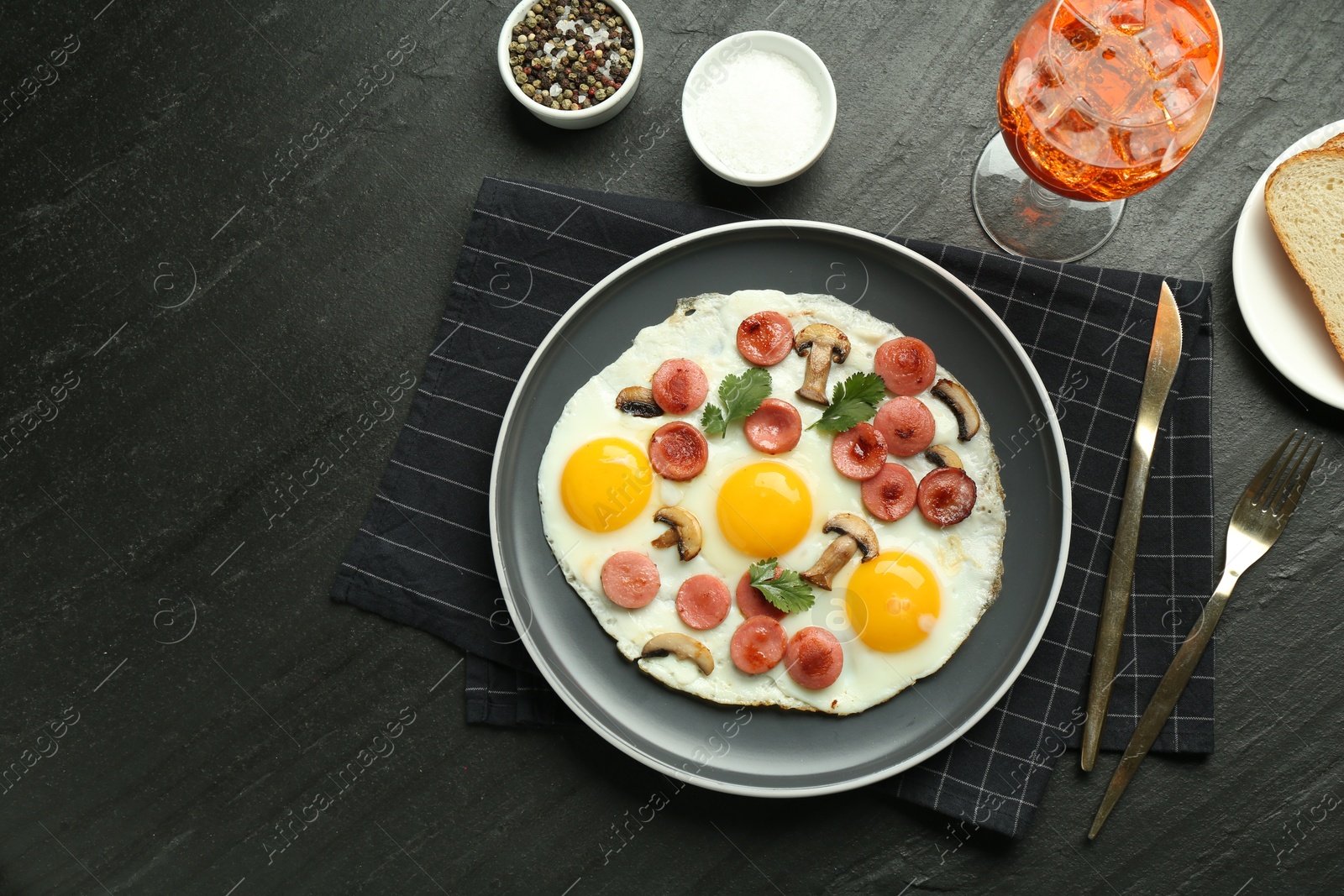 Photo of Tasty brunch. Delicious fried eggs with sausage, mushrooms and aperol cocktail served on black table, flat lay. Space for text