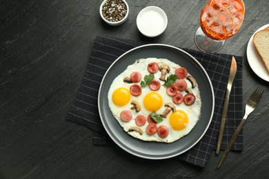 Photo of Tasty brunch. Delicious fried eggs with sausage, mushrooms and aperol cocktail served on black table, flat lay. Space for text