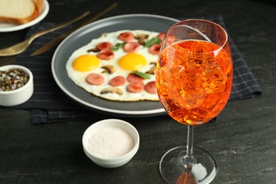 Photo of Tasty brunch. Aperol cocktail, delicious fried eggs with sausage served on black table, closeup