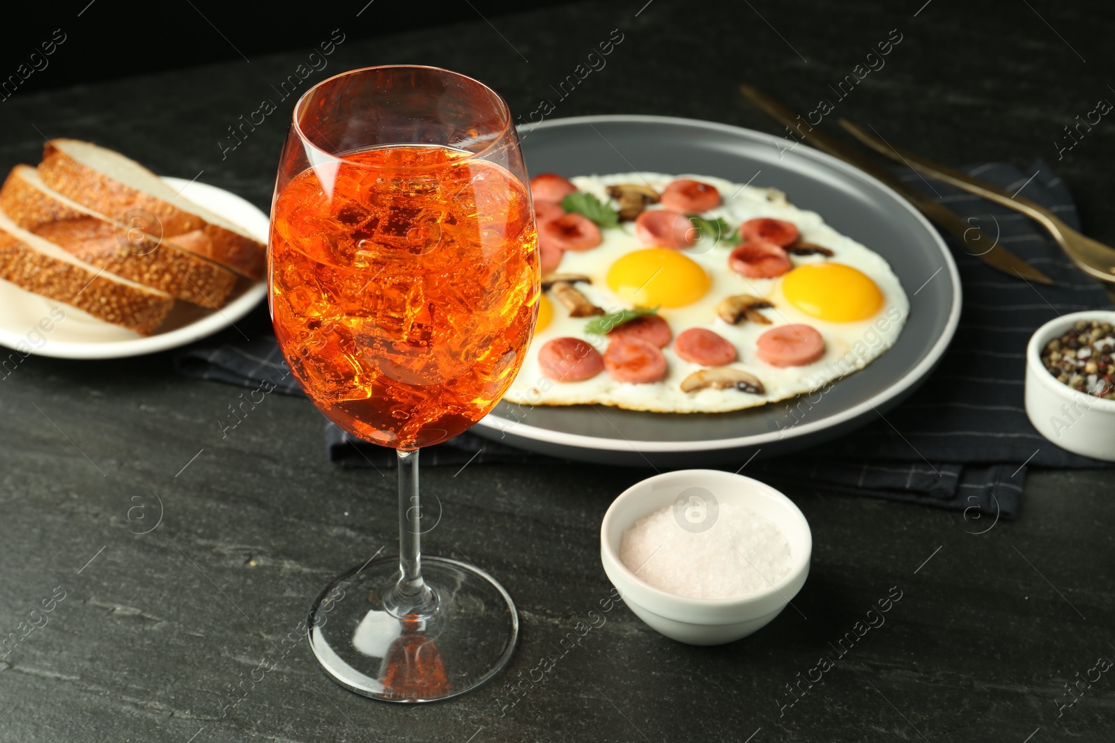 Photo of Tasty brunch. Aperol cocktail, delicious fried eggs with sausage served on black table, closeup