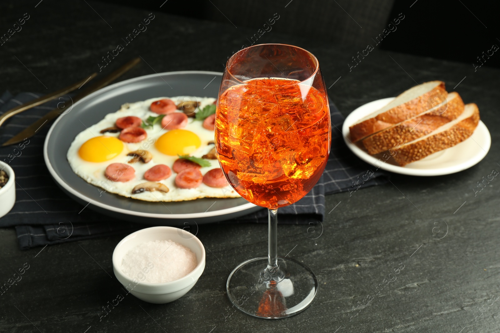 Photo of Tasty brunch. Aperol cocktail, delicious fried eggs with sausage served on black table, closeup