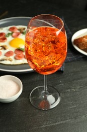 Photo of Tasty brunch. Aperol cocktail, delicious fried eggs with sausage served on black table, closeup