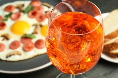 Photo of Tasty brunch. Aperol cocktail, delicious fried eggs with sausage served on black table, closeup