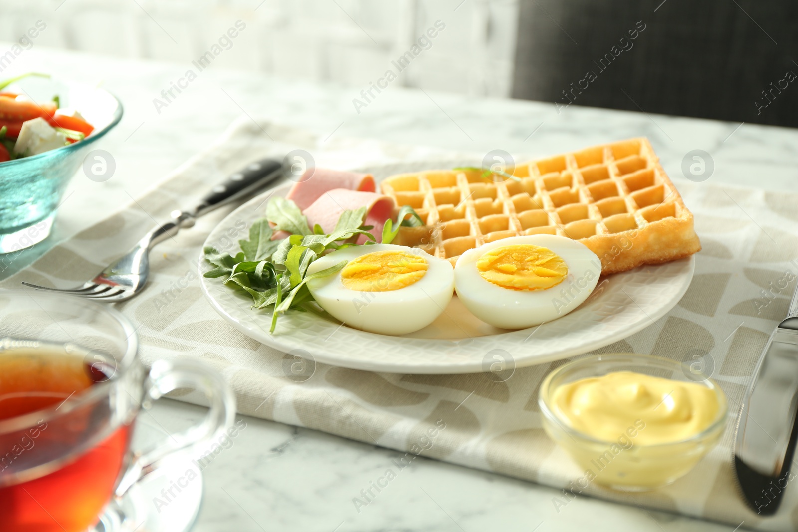 Photo of Tasty brunch. Boiled egg, Belgian waffle, arugula, ham and sauce on white marble table