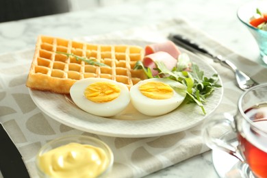 Photo of Tasty brunch. Boiled egg, Belgian waffle, arugula, ham and sauce on light table, closeup