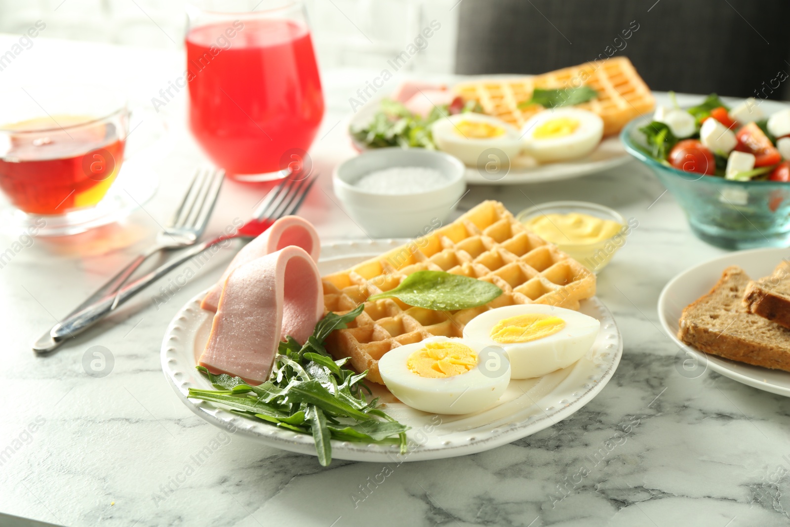 Photo of Tasty brunch. Boiled egg, Belgian waffle, arugula and ham on white marble table