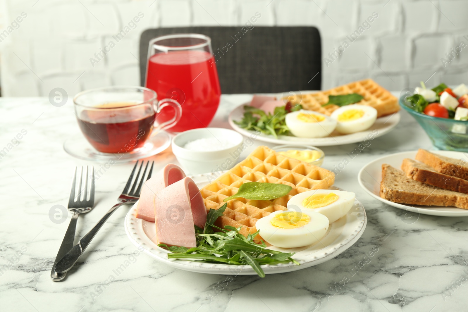 Photo of Tasty brunch. Boiled egg, Belgian waffle, arugula and ham on white marble table