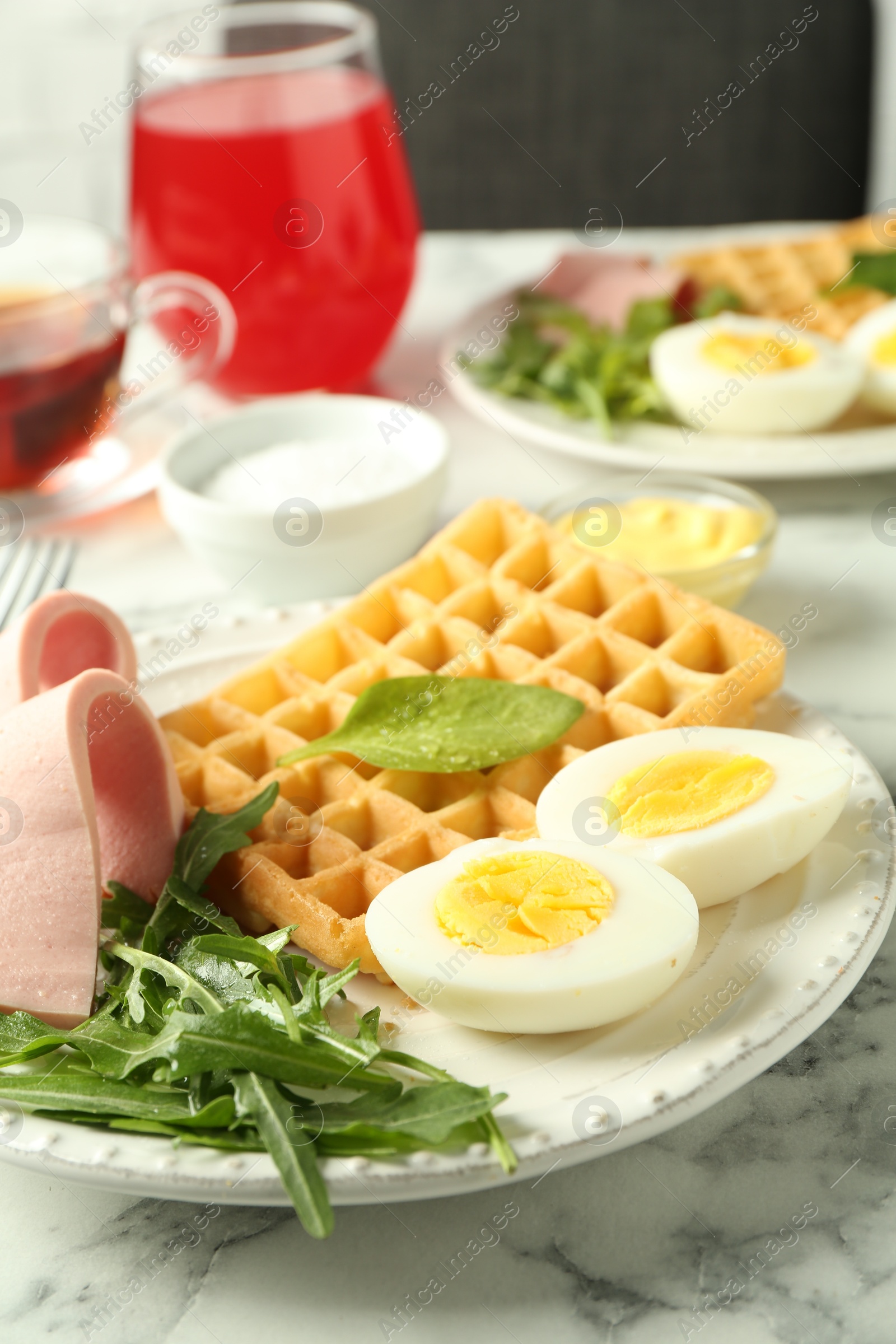 Photo of Tasty brunch. Boiled egg, Belgian waffle, arugula and ham on white marble table, closeup