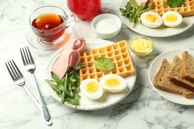 Photo of Tasty brunch. Boiled egg, Belgian waffle, arugula and ham served on white marble table