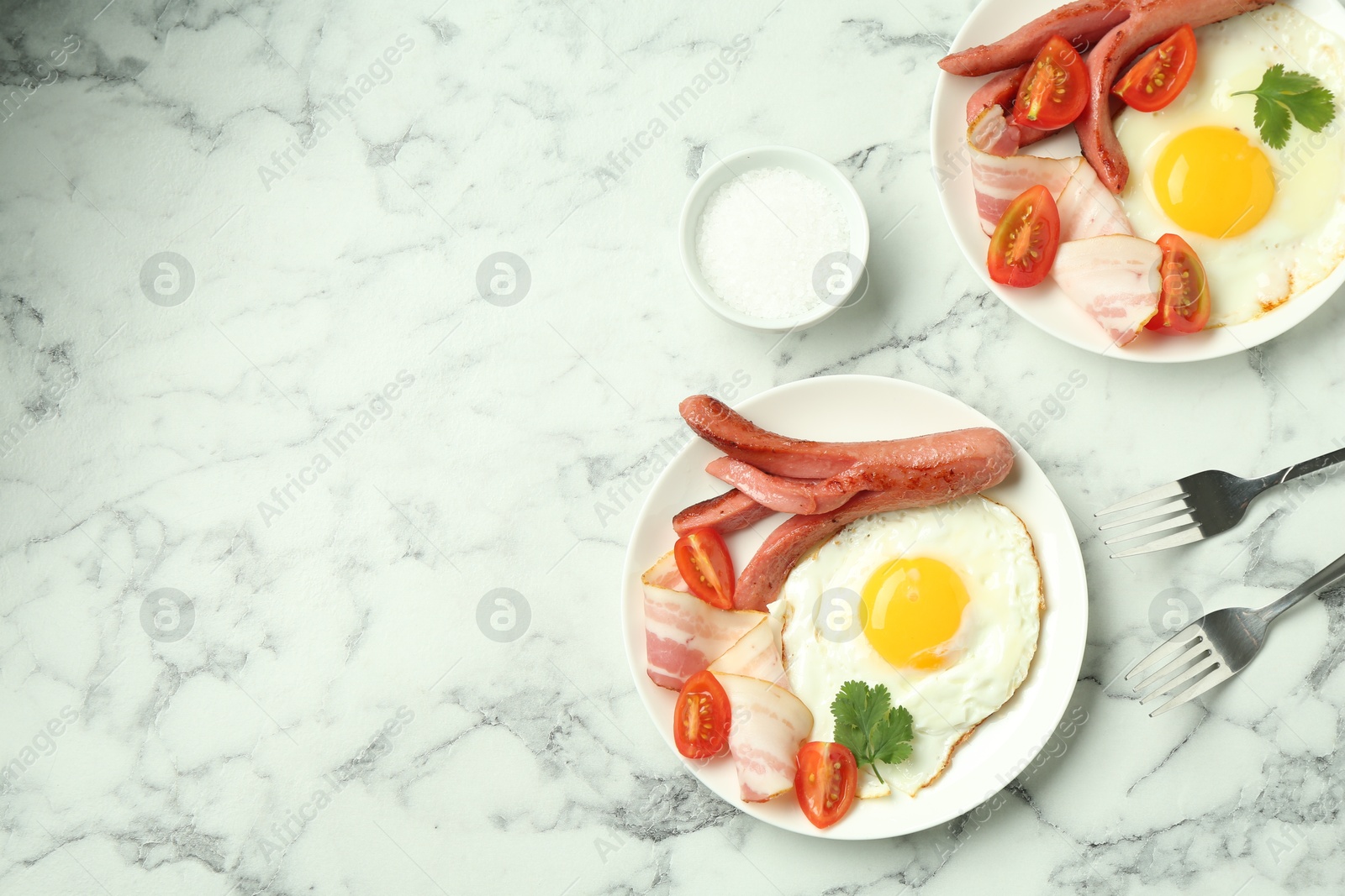 Photo of Tasty brunch. Fried eggs, sausage, bacon and tomatoes served on white marble table, flat lay. Space for text