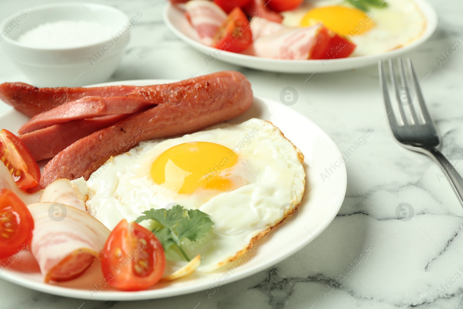 Photo of Tasty brunch. Fried egg, sausage, bacon and tomatoes on white marble table, closeup