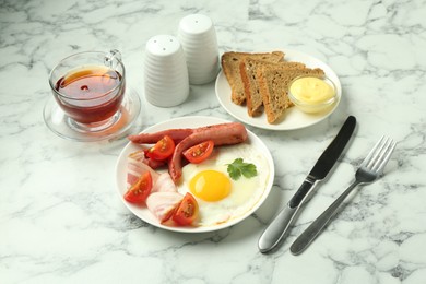 Photo of Tasty brunch. Fried egg, sausage, bacon and tomatoes served on white marble table