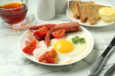 Photo of Tasty brunch. Fried egg, sausage, bacon and tomatoes on white marble table, closeup